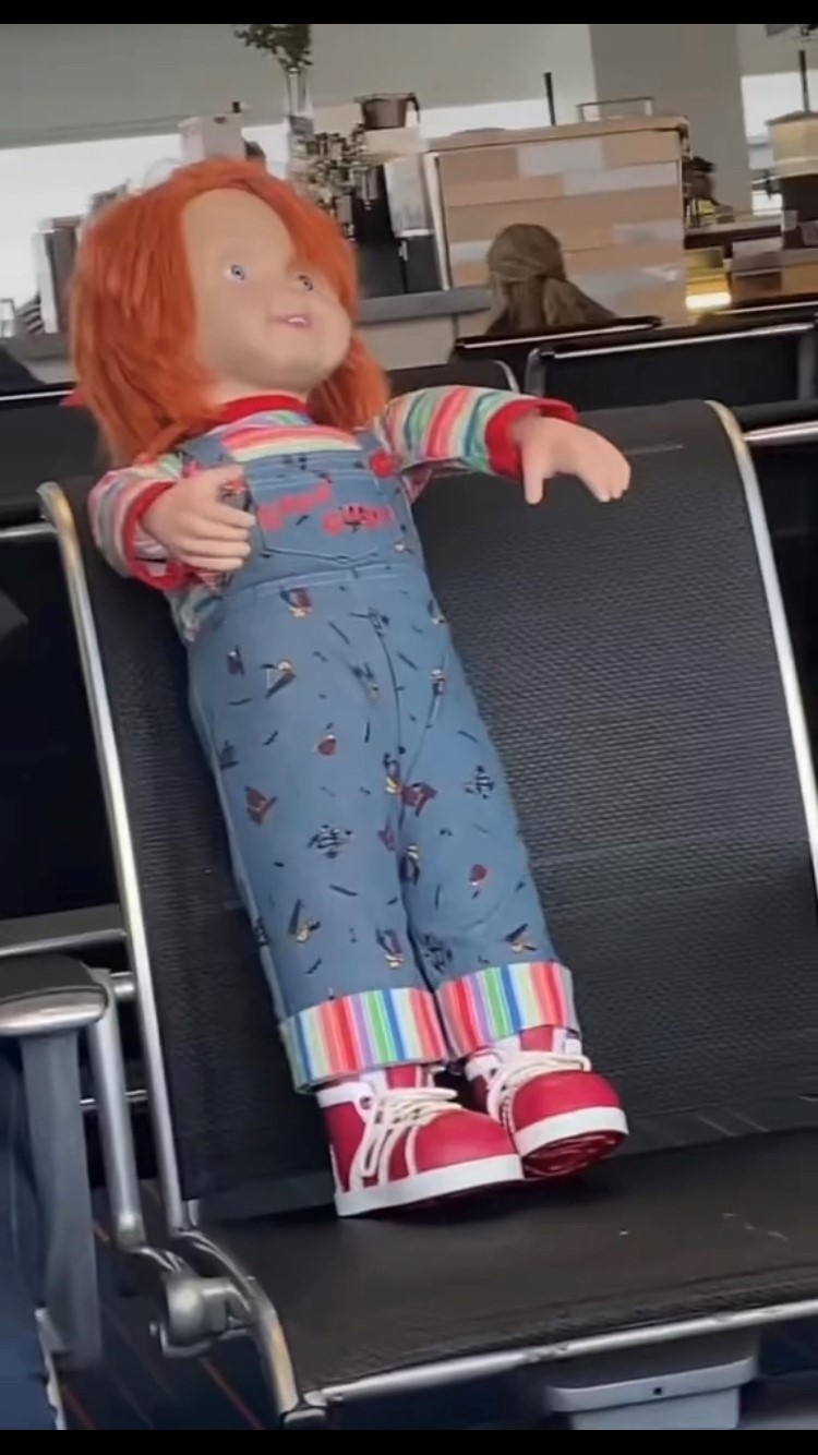 A chucky doll in an airport seat.