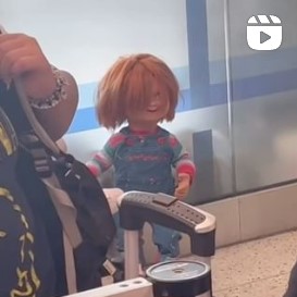 A Chucky Doll standing alone at an airport.