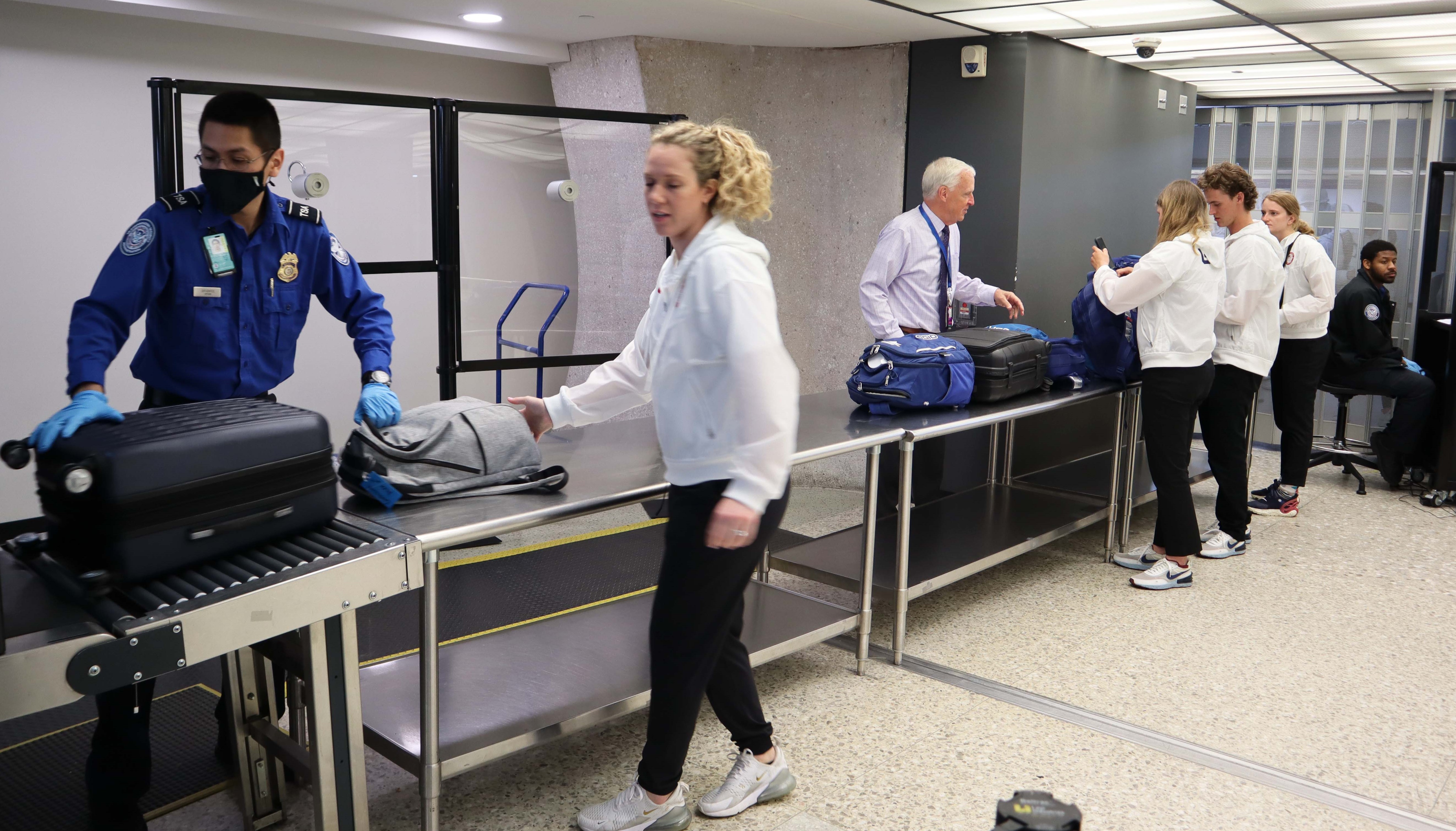 TSA Officer Luciano Sifuentes screens a U.S. Olympian at a Washington Dulles International Airport checkpoint. Dulles Federal Security Director Scott T. Johnson (white shirt, tie) engages with several Olympians preparing their carry-on bags for X-ray screening. (Photo by Sena Park)