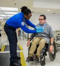 A TSA officer performs a pat down on a passenger in a wheelchair