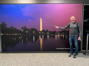 TSA Director of Staffing & Scheduling Michael Coffman poses in front of one of his pictures on display at the Dulles International Airport baggage claim. (Photo by Michael Coffman)