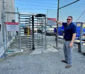 Supervisory TSI Robert Hoppa points out an airport employee entry gate to the AOA, which has a keypad, barbed wire, high fencing and a personnel gate that requires employees to use a keypad and a badge to gain entry. (Photo by Lisa Farbstein)